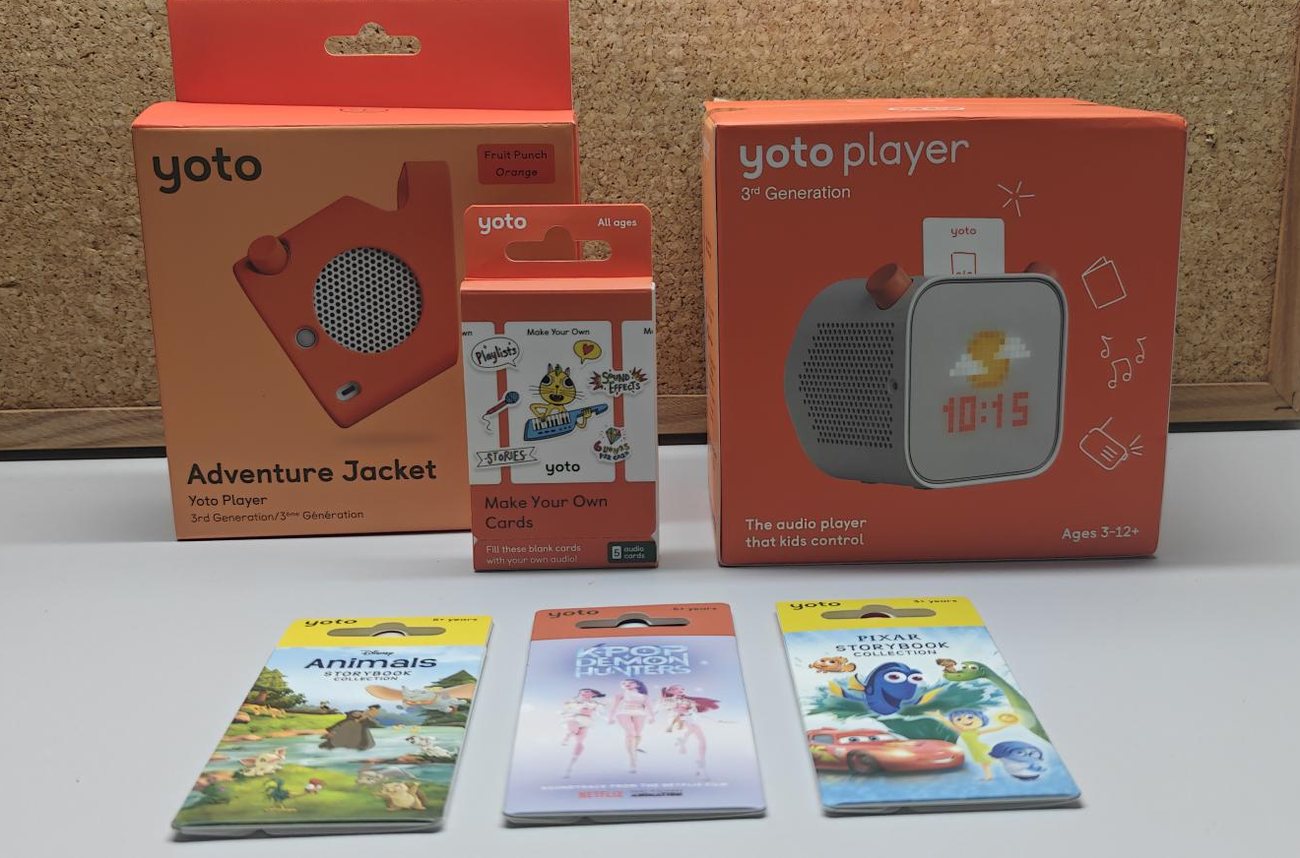 A real photo of the actual prize bundle on a desk: the Yoto Player 3rd Generation box, the Fruit Punch Adventure Jacket, the Make Your Own pack, and the Disney Animals, KPop Demon Hunters and Disney Pixar cards